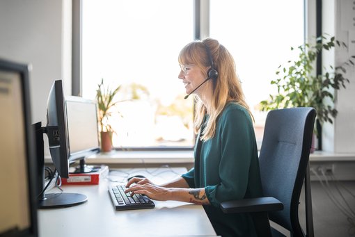 Gamification Contact Center Side view of young female customer service representative using computer at desk in brightly lit office
