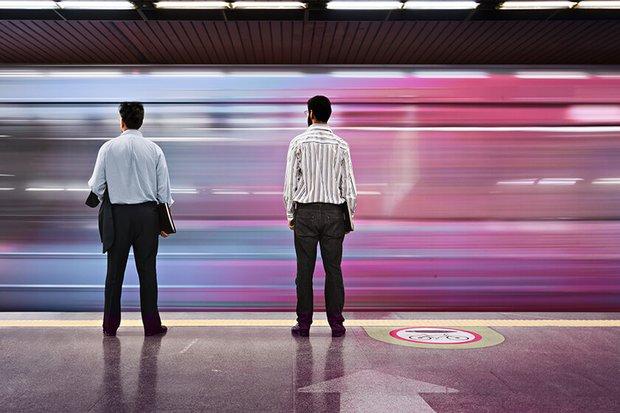 two men standing on platform while train rushes past two men standing on platform while train rushes past