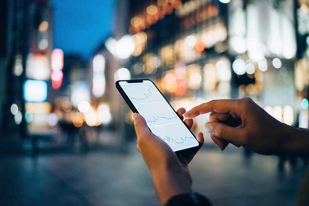 Businesswoman Reading Smartphone Businesswoman reading financial trading data on smartphone in downtown city street against illuminated urban skyscrapers